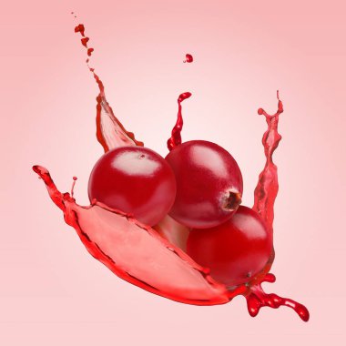 Lezzetli olgun kızılcıklar ve soluk kırmızı arka planda havaya su sıçratan sıvılar.