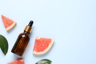 Şişede greyfurt yağı, yapraklar ve açık mavi masada meyve kesimi. Metin için boşluk