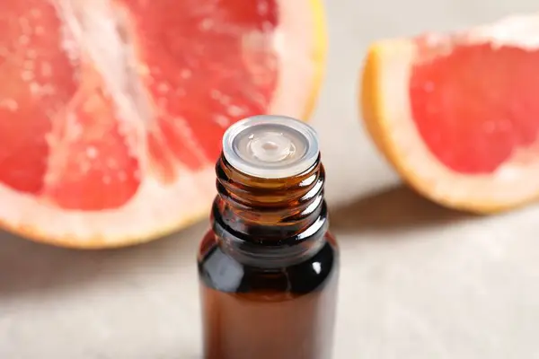 Grapefruit essential oil in bottle and fruit on light table, closeup