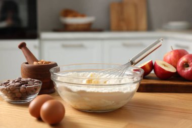 Yemek pişirme süreci. Metal çırpma, kase, un, yumurta ve diğer ürünler mutfaktaki ahşap masada, yakın plan.