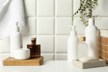 Duvarın yanındaki beyaz masada farklı banyo aksesuarları ve kişisel bakım ürünleri var.
