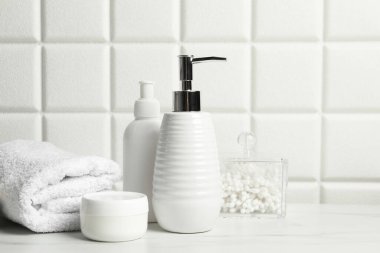 Duvarın yanındaki beyaz masada farklı banyo aksesuarları ve kişisel bakım ürünleri var.