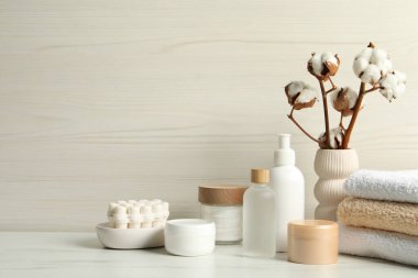 Banyo aksesuarları. Kişisel bakım ürünleri ve vazodaki pamuk çiçekleri beyaz mermer masada, tahta duvarın yanında.