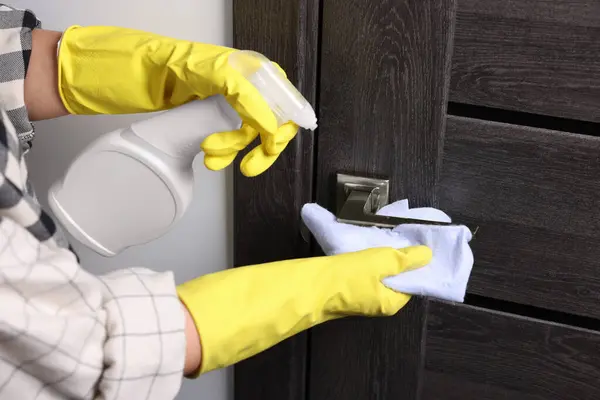 Woman cleaning door handle with detergent and rag indoors, closeup