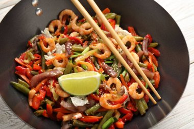 Karides kızartması, tavada sebzeler ve hafif ahşap masada çubuklar, yakın plan.