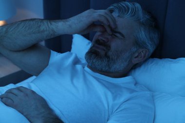 Yetişkin bir adam gece yatağında baş ağrısı çekiyor.