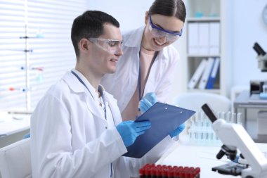 İçerideki masada laboratuvar test formlarıyla çalışan bilim adamları.