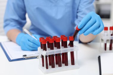 Laboratuvar testi. Kapalı alandaki beyaz masada tüplerde kan örnekleri olan bir doktor.