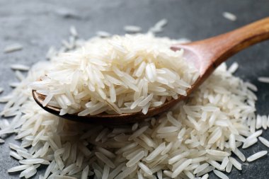 Çiğ basmati pilavı ve tahta kaşık siyah masada, yakın plan.
