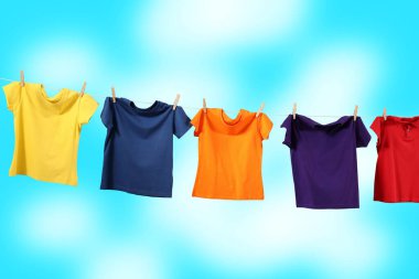 Mavi gökyüzüne karşı çamaşır ipinde kuruyan renkli tişörtler.