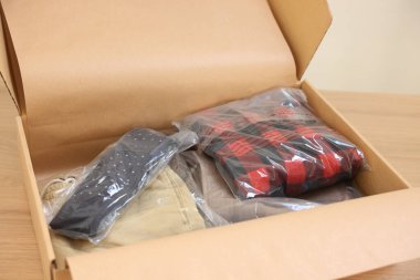 Tahta masadaki plastik poşetlerde farklı giysiler olan karton kutuyu aç. Teslimat servisi