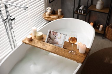 Tabletli ahşap tepsi, banyo küvetinde şarap ve mumlar.