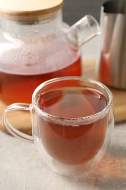 Cam bardakta Aromatik çay ve açık gri masada çaydanlık, yakın plan.