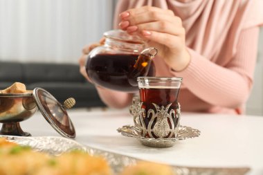 Beyaz masada çaydanlıktan fincana lezzetli Türk çayı döken kadın, yakın plan.