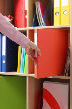 Kadın raflardan klasör ofis klasörünü alıyor, yakın plan.