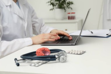 Endocrinologist working at table, focus on stethoscope and model of thyroid gland clipart