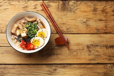 Erişte çorbası. Tahta masanın üstünde bir kase lezzetli ramen ve çubuk, üst manzara. Metin için boşluk