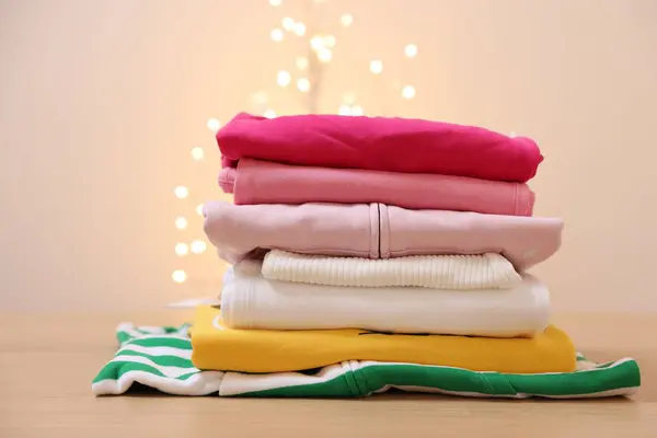 Stack of folded clothes on wooden table against beige background with blurred lights