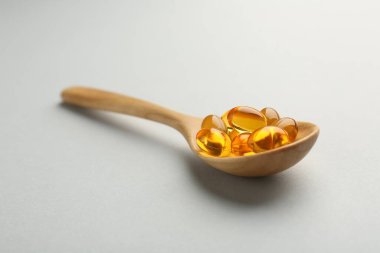Vitamin kapsülleri tahta kaşıkta açık gri arka planda, yakın plan. Sağlık takviyesi
