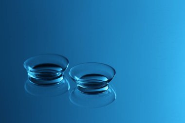 Ayna yüzeyinde bir çift kontakt lens, mavi tonda. Metin için boşluk