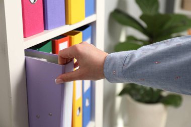 İçerideki raflardan klasör ofis klasörünü alan kadın.