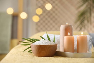Spa kompozisyonu. Yumuşak sarı yüzeyde yanan mumlar, deniz tuzu ve havlu, metin için alan