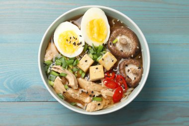 Açık mavi ahşap masada bir kase lezzetli ramen, üst manzara. Erişte çorbası.