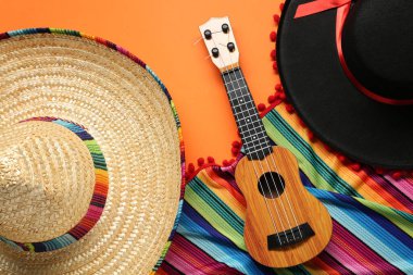 Meksika sombrero şapkası, gitar ve turuncu arka planda renkli panço.