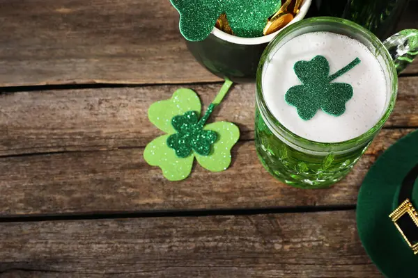 St. Patrick 'in gündüz partisi. Yeşil bira, leprikon şapka, altın küpü ve tahta masa üzerindeki dekoratif yonca yaprakları. Metin için boşluk