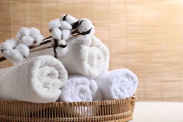 Rolled soft towels and cotton branch on white table indoors, space for text