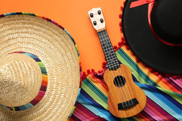 Meksika sombrero şapkası, gitar ve turuncu arka planda renkli panço.