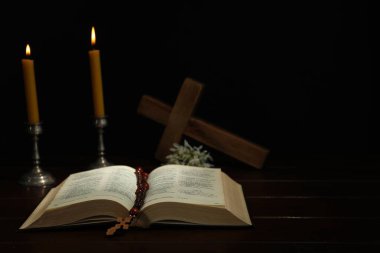 Haçlar, tespih boncukları, ahşap masada İncil ve kilise mumları.