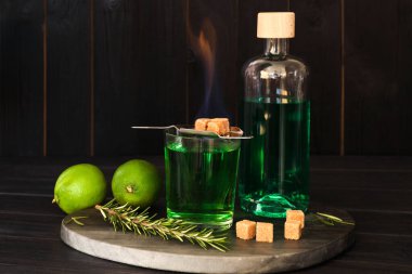 Bardakta absent, alevli kahverengi şeker, biberiye ve ahşap masada limon. Alkolik içki.