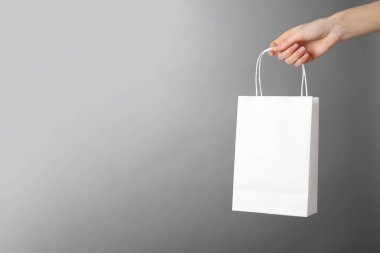 Gri arka planda beyaz kağıt poşet tutan bir kadın, mesaj için yeri olan yakın plan. Tasarım için model