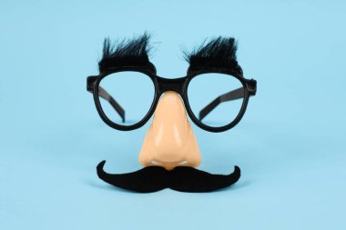 Sahte bıyıklı komik maske, açık mavi arka planda burun ve gözlük.
