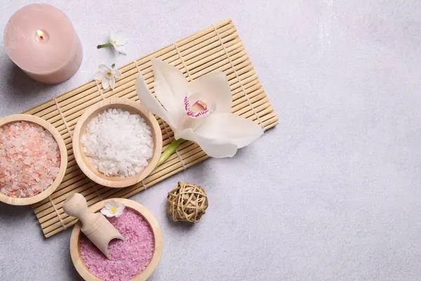 Açık gri masa üzerinde farklı spa ürünleri ve orkide içeren düz bir kompozisyon. Metin için boşluk