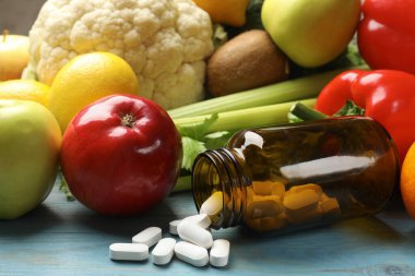 Beslenme takviyeleri. Açık mavi ahşap masada, gıda ürünlerinin yanında haplarla çevrilmiş bir şişe.