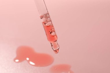 Pembe arka plandaki pipetten damlayan nemlendirici serum, yakın plan.