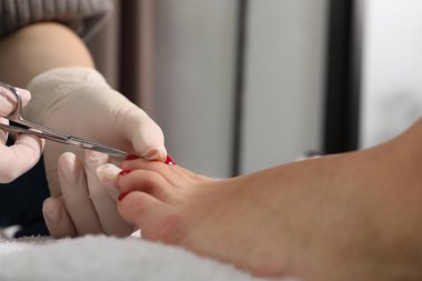 Güzellik salonunda pedikür uzmanı, müşterinin ayak tırnaklarını makasla kesiyor.
