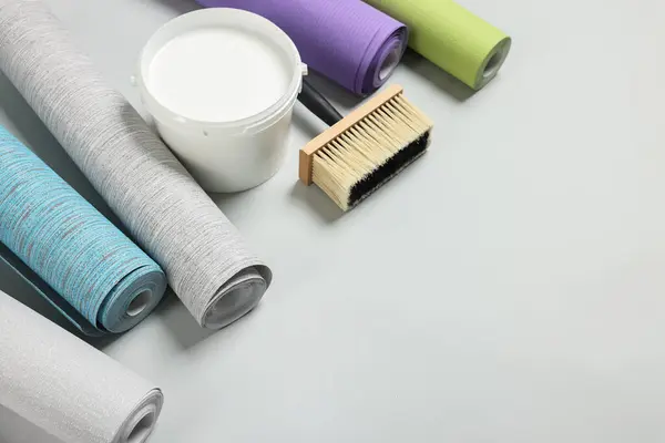Different wallpaper rolls, brush and bucket with glue on light grey background, above view. Space for text