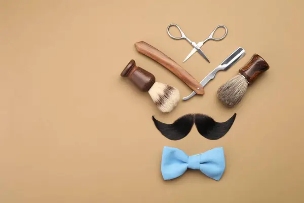Artificial moustache and barber tools on beige background, flat lay. Space for text