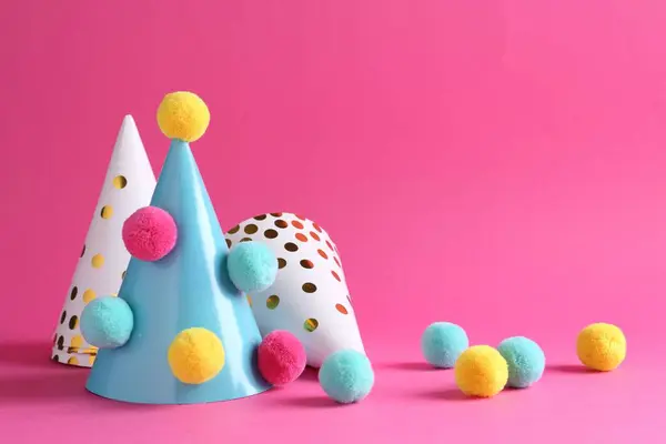 Party hats with color pompoms on pink background
