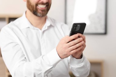 Ofiste akıllı telefon kullanan gülümseyen adam, yakın plan.