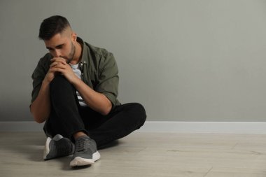 Açık gri duvarın yanında yerde oturan üzgün adam. Metin için boşluk