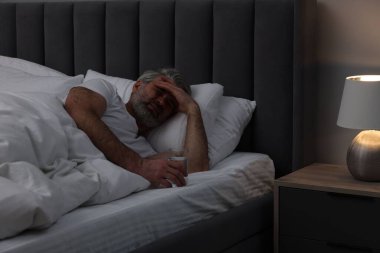 Yetişkin bir adam gece yatağında baş ağrısı çekiyor.