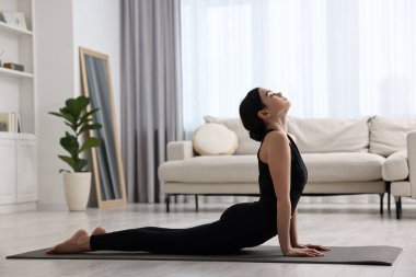 Evde yoga minderinde kobra asana egzersizi yapan bir kız. Bhujangasana pozu