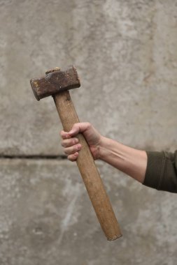 Gri duvarın yanında balyozlu bir adam, yakın plan.