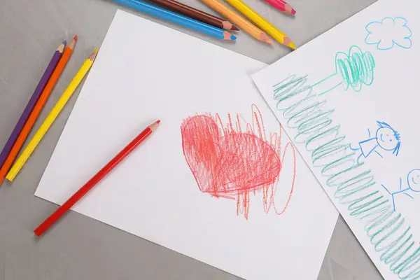 Cute children`s drawings and colorful pencils on grey table, flat lay