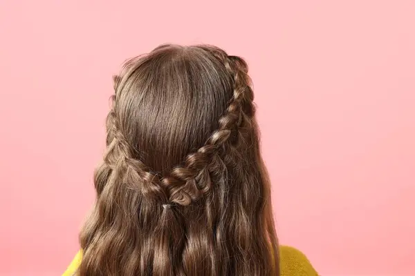 Little girl with braided hair on pink background, back view