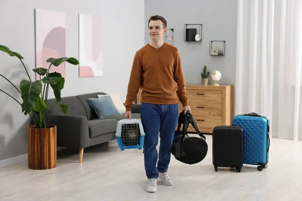 Travel with pet. Man holding carrier with cute cat and bag at home